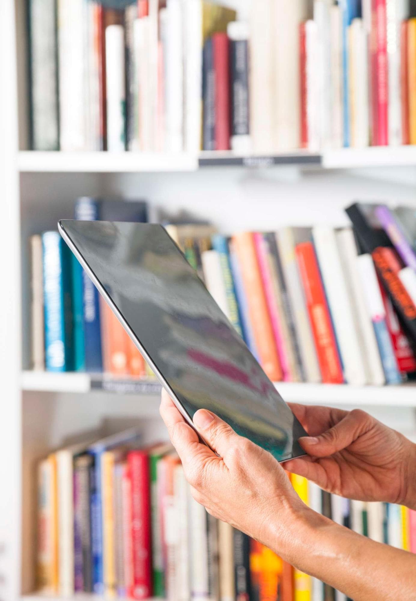Person using a tablet with a  shelf of books in background