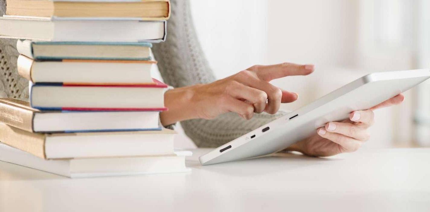 Women using tablet with stack of books